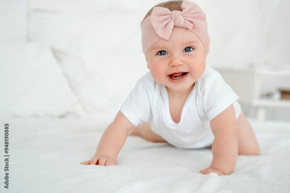 A baby girl is smiling at home on a white bed with a bow on her head, a happy healthy child of six months is laughing A baby girl is smiling at home on a white bed with a bow on her head, a happy healthy child of six months is laughing