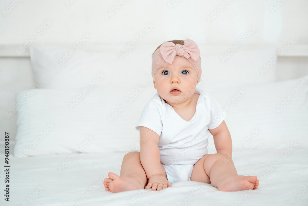 A baby girl is smiling at home on a white bed with a bow on her head, a happy healthy child of six months is laughing A baby girl is smiling at home on a white bed with a bow on her head, a happy healthy child of six months is laughing