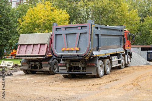 Two large dump trucks are parked next to each other on a dirt road