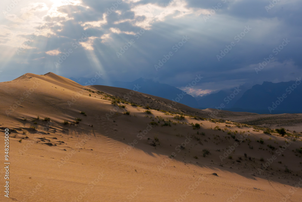 Dramatic desert dunes under sunbeams and cloudy sky