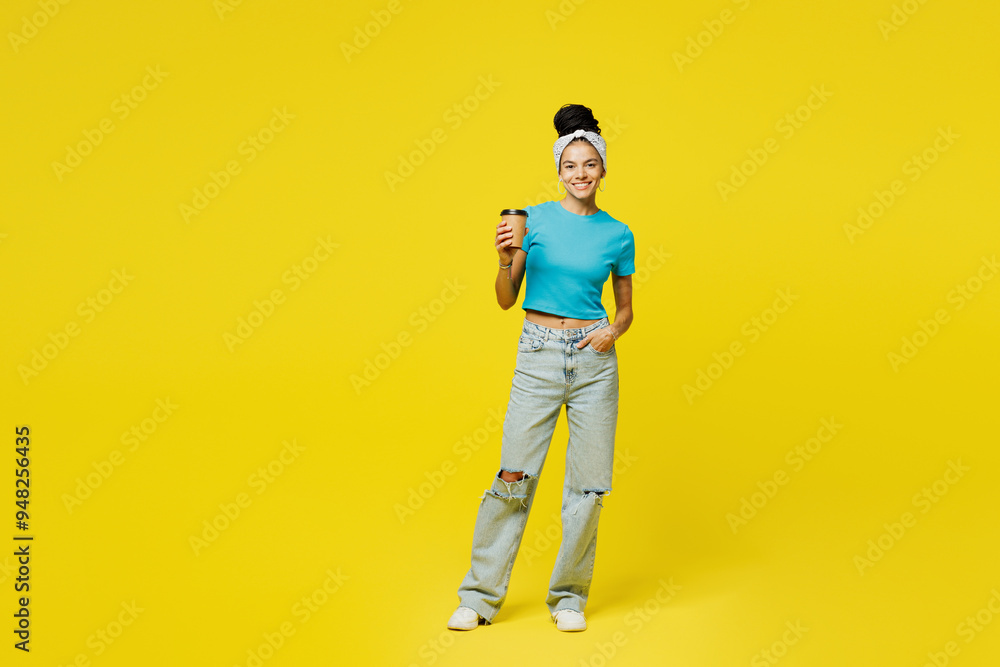Fototapeta premium Full body young Latin woman she wears blue top t-shirt headband casual clothes hold takeaway delivery craft paper brown cup coffee to go isolated on plain yellow background studio. Lifestyle concept.