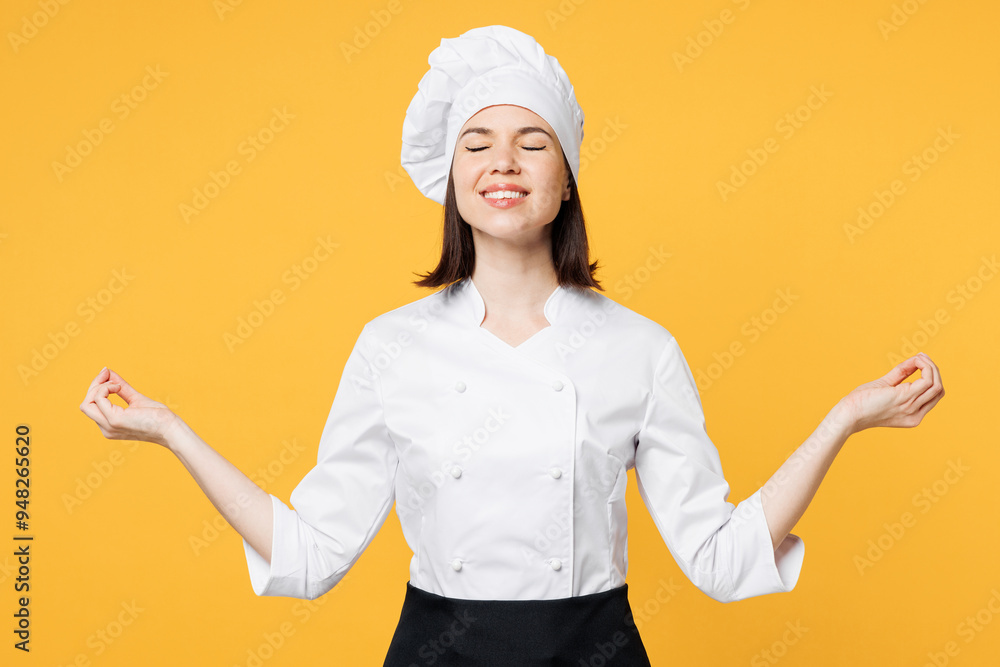 Young chef cook baker woman she wear white shirt black apron uniform toque chefs hat hold hands in yoga om aum gesture relax meditate isolated on plain yellow background studio. Cooking food concept. Young chef cook baker woman she wear white shirt black apron uniform toque chefs hat hold hands in yoga om aum gesture relax meditate isolated on plain yellow background studio. Cooking food concept.