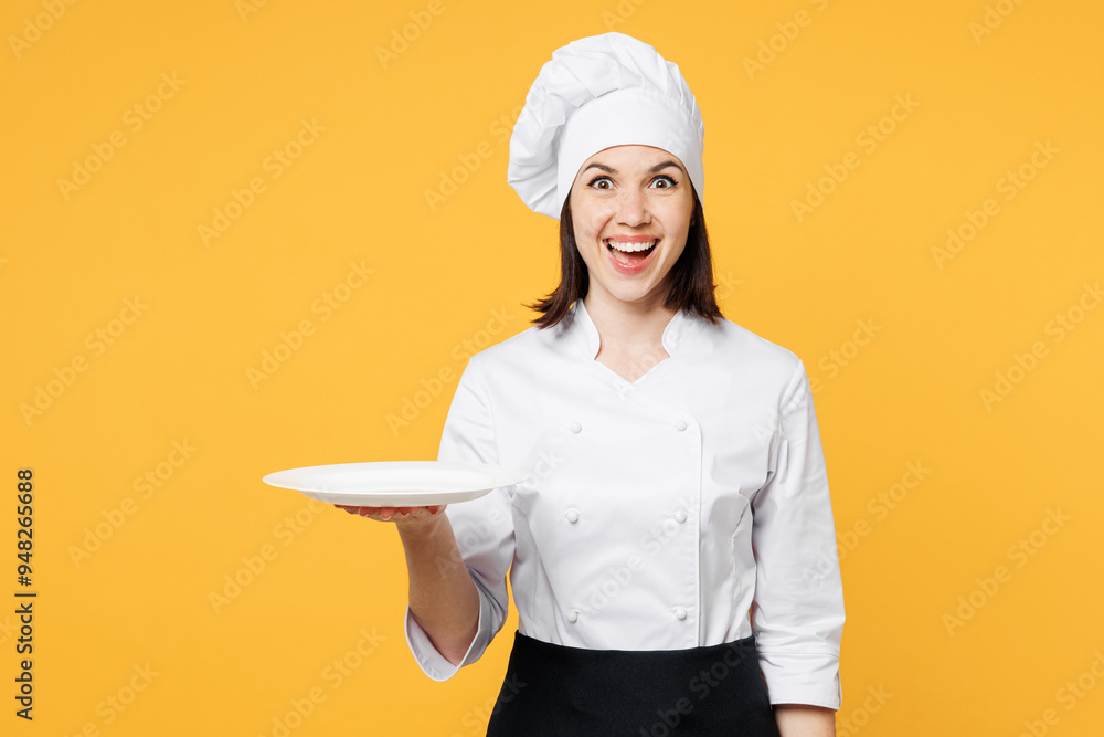 Young surprised shocked excited chef cook baker woman wear white shirt black apron uniform toque chefs hat hold in hand empty plate isolated on plain yellow background studio. Cooking food concept. Young surprised shocked excited chef cook baker woman wear white shirt black apron uniform toque chefs hat hold in hand empty plate isolated on plain yellow background studio. Cooking food concept.