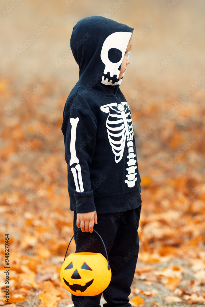 Creepy skeleton costume for Halloween for a kid. Boy with a scary carnival costume with a skull and bones holding orange pumpkin bucket. All saint day concept. Creepy skeleton costume for Halloween for a kid. Boy with a scary carnival costume with a skull and bones holding orange pumpkin bucket. All saint day concept.