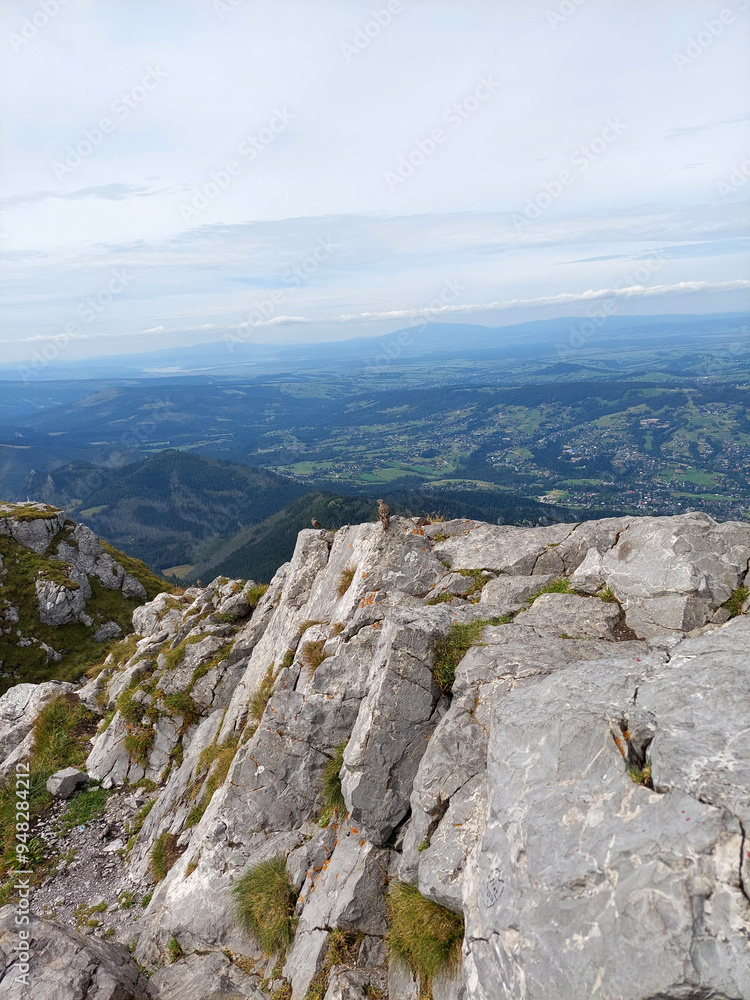 Fototapeta premium Standing on a rocky mountain peak with a view of distant mountains and valleys below