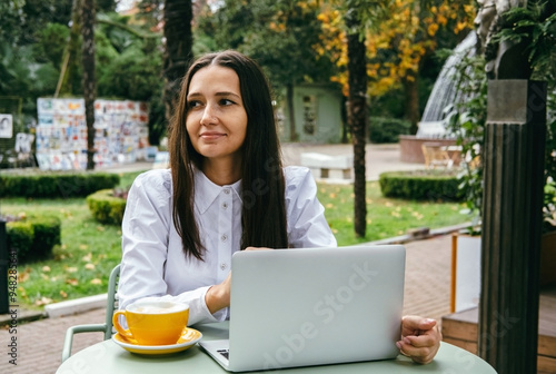 A beautiful millennial woman works remotely in a cafe on a laptop.