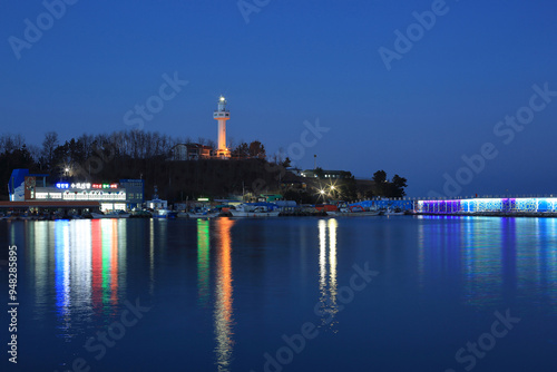 Goseong-gun, Gangwon-do, South Korea - January 21, 2022: Night view of Daejin Lighthouse with illumination at Daejin Port with moored fishing boats and fish market photo