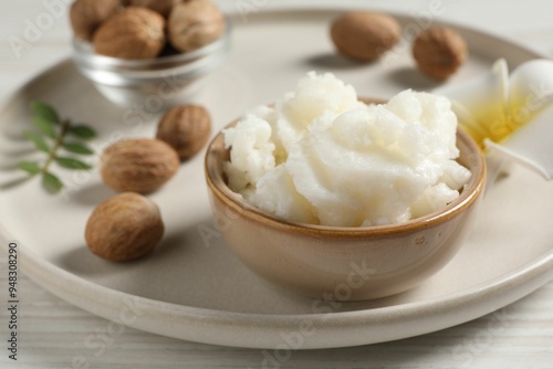 Shea butter in bowl, flower and nuts on white wooden table, closeup