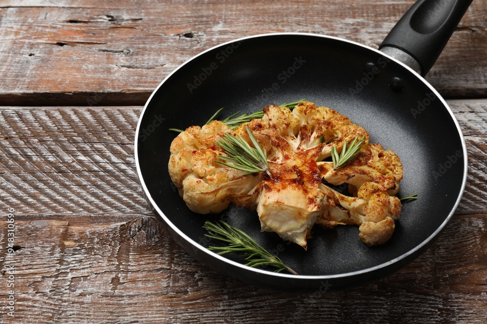 Tasty cauliflower steak and rosemary in frying pan on wooden table, closeup Tasty cauliflower steak and rosemary in frying pan on wooden table, closeup