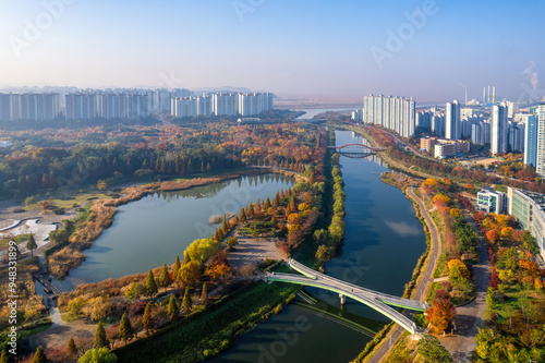 Sangnok-gu, Ansan-si, Gyeonggi-do, South Korea - November 3, 2021: Aerial and morning view of Ansan Lake Park with a bridge and trail against high-rise apartments in the background in autumn