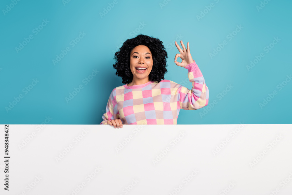 Photo of attractive young woman stand behind white empty space okey dressed stylish pink plaid clothes isolated on blue color background Photo of attractive young woman stand behind white empty space okey dressed stylish pink plaid clothes isolated on blue color background