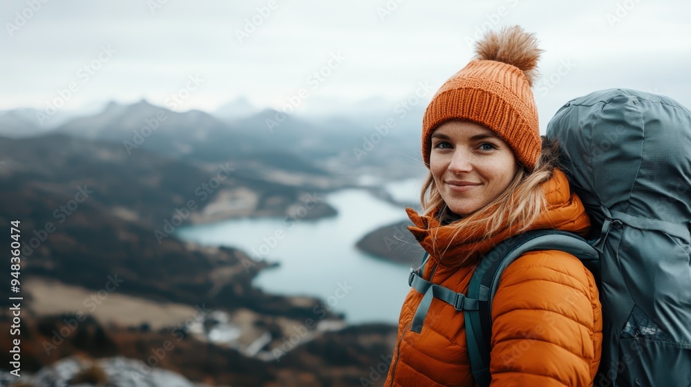 A smiling woman in an orange jacket and beanie hikes with a large backpack, overlooking a picturesque lake and mountains backdrop, showing adventure and joy. A smiling woman in an orange jacket and beanie hikes with a large backpack, overlooking a picturesque lake and mountains backdrop, showing adventure and joy.