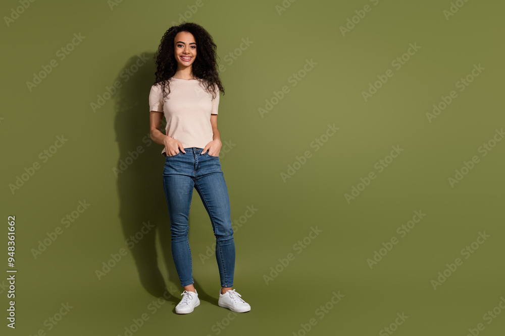 Full size photo of cool positive girl dressed beige t-shirt jeans hold arms in pockets near empty space isolated on khaki color background Full size photo of cool positive girl dressed beige t-shirt jeans hold arms in pockets near empty space isolated on khaki color background