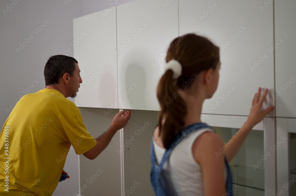 A father and a daughter are working together to install new cabinets A father and a daughter are working together to install new cabinets