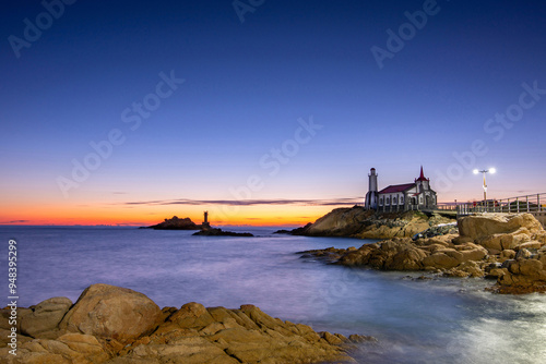 Jukseong-ri, Gijang-gun, Busan, South Korea - January 2, 2022: Long exposure and night view of Jukseong Cathedral with rocks and lighthouse on the sea photo