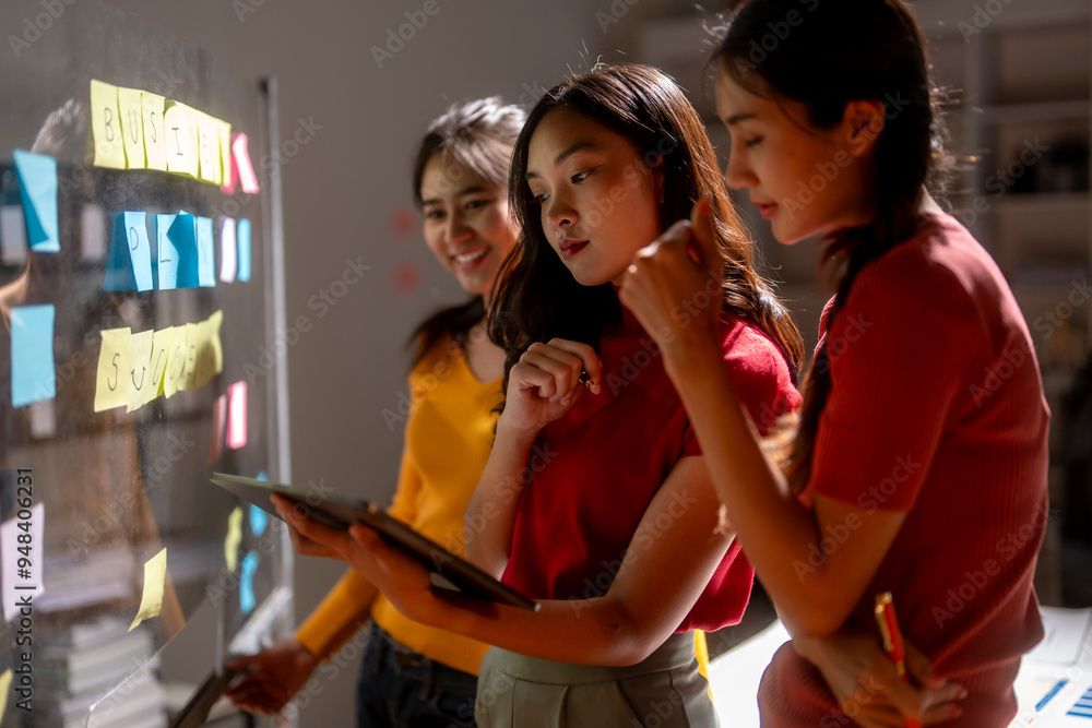 Obraz premium Three young businesswomen are working together in the office using a digital tablet and brainstorming