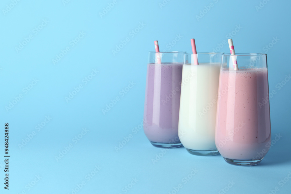 Different tasty yogurts and straws in glasses on light blue background, space for text Different tasty yogurts and straws in glasses on light blue background, space for text
