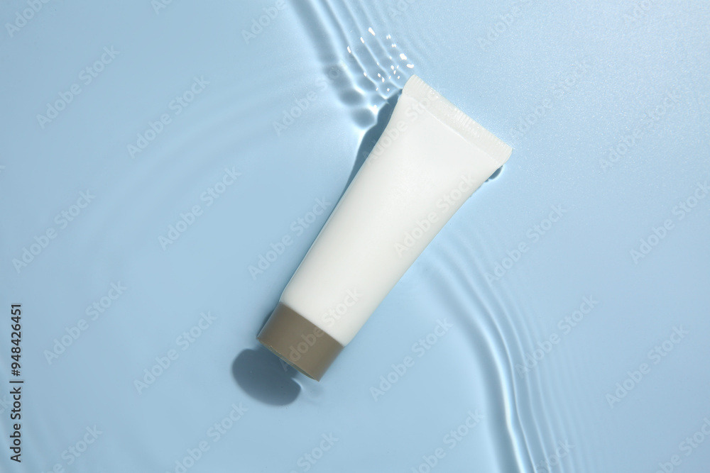 Cosmetic product. Tube with cream in water on light blue background, top view Cosmetic product. Tube with cream in water on light blue background, top view