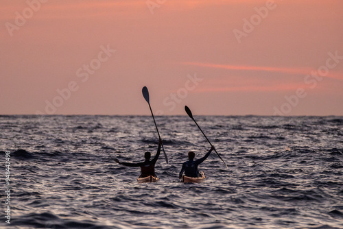 Dos hombres en dos kayaks levantando los remos. Deporte en el mar antes del amanecer, en la alba. photo