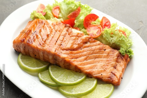 Delicious grilled salmon fillet with vegetable salad and lime on grey table, closeup