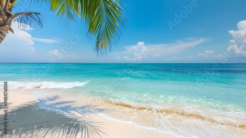 A panoramic view of a tropical beach with a palm tree frond in the foreground, white sand, azure water and blue sky with clouds.