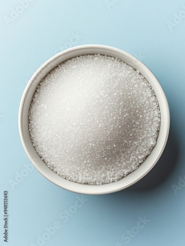 White granulated sugar in a white bowl on a blue background.