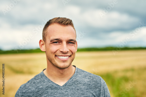Man, smile and portrait in countryside for travel, journey and stretching legs on road trip. Person, happy and relax at wheat field for freedom, summer vacation and adventure in Germany for holiday