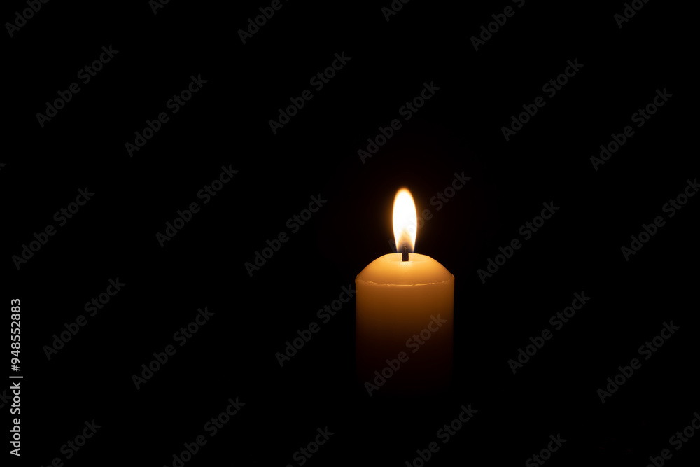 A single burning candle flame or light glowing on a big white candle isolated on red or dark background on table in church for Christmas, funeral or memorial service A single burning candle flame or light glowing on a big white candle isolated on red or dark background on table in church for Christmas, funeral or memorial service