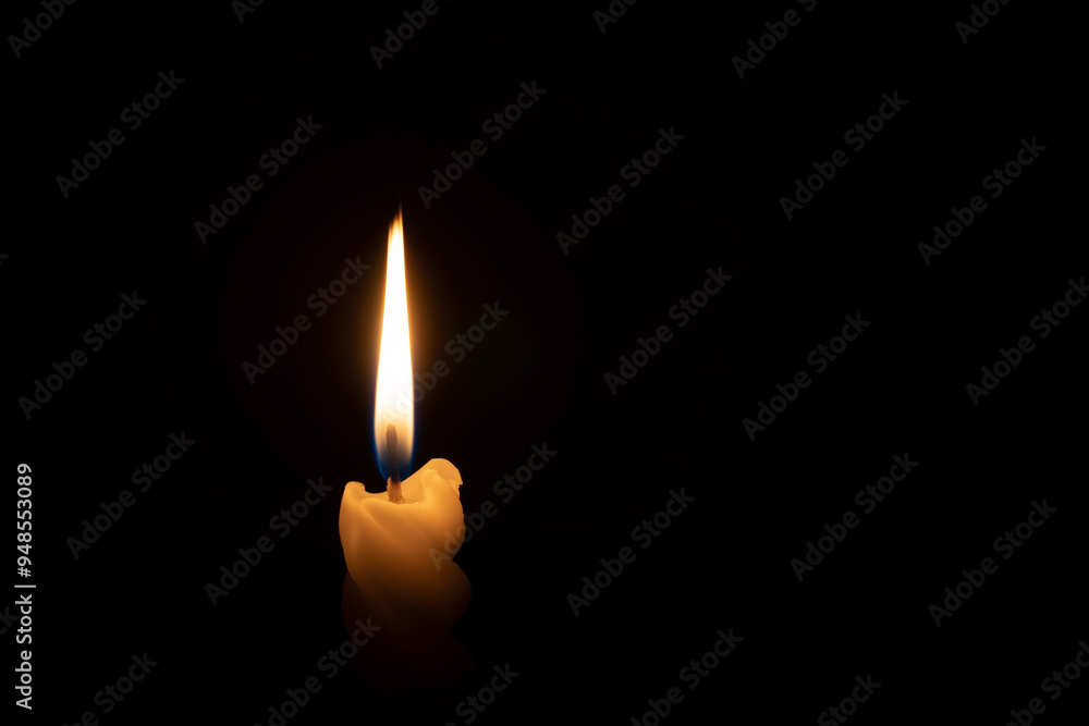 A single burning candle flame or light glowing on a spiral white candle on black or dark background on table in church for Christmas, funeral or memorial service with copy space A single burning candle flame or light glowing on a spiral white candle on black or dark background on table in church for Christmas, funeral or memorial service with copy space