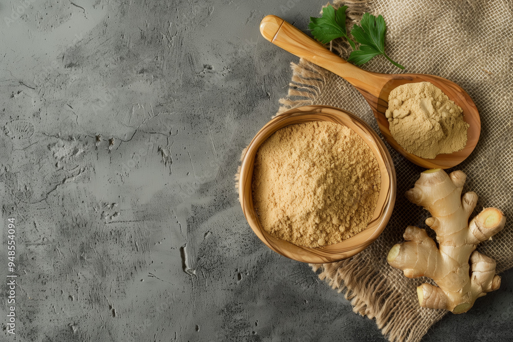 Top view of ginger powder in a bowl and a fresh ginger root on a burlap cloth with a wooden spoon over a grey concrete background. Top view of ginger powder in a bowl and a fresh ginger root on a burlap cloth with a wooden spoon over a grey concrete background.