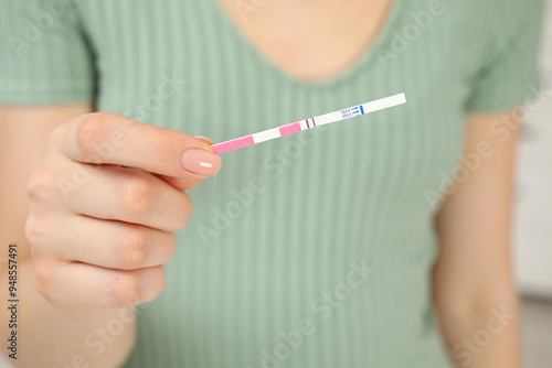 Woman holding positive pregnancy test indoors, closeup view