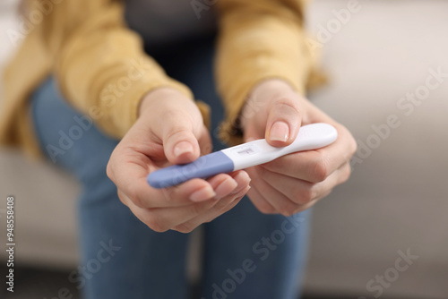 Woman holding pregnancy test on sofa indoors, closeup