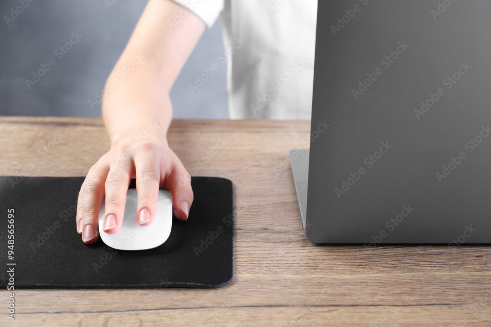 Fototapeta premium Woman using computer mouse while working with laptop at wooden table, closeup