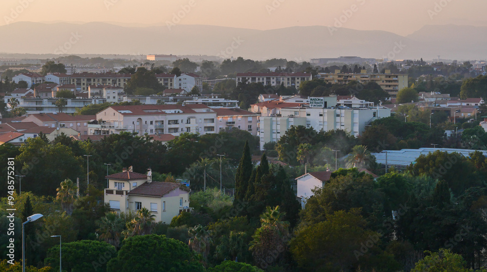 Fototapeta premium View of the city of Perpignan, France, sunset, haze, red roofs, houses, trees, life, vacation, postcard, Europe, mountain silhouettes, calm, beauty