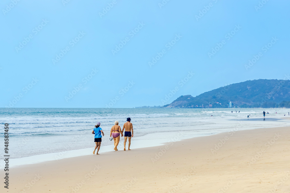 Young woman running with elderly couple walking on beach. Active and happy woman in active sportswear with hat enjoy jogging behind senior lovers on beach. Fitness girl with family exercise together. Young woman running with elderly couple walking on beach. Active and happy woman in active sportswear with hat enjoy jogging behind senior lovers on beach. Fitness girl with family exercise together.