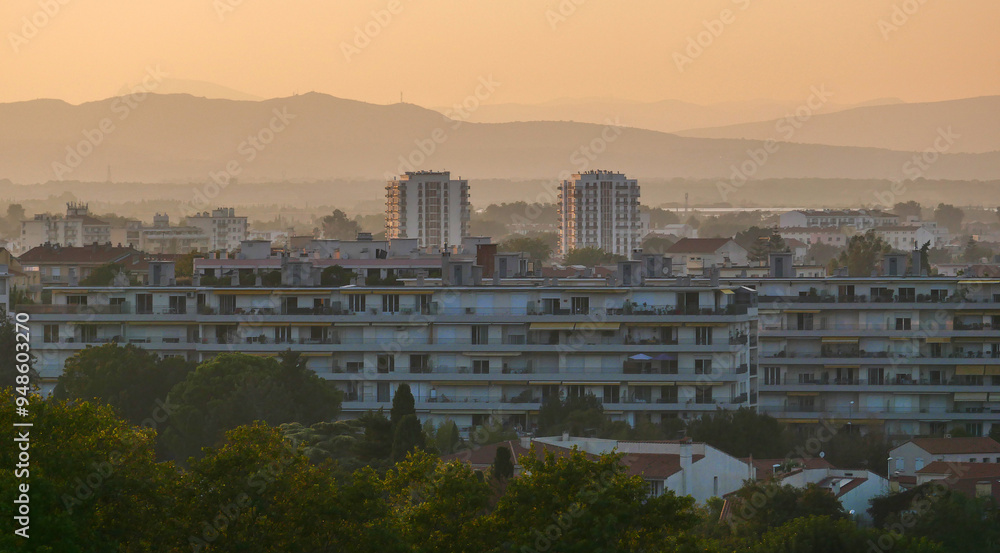 Obraz premium Evening view of the city of Perpignan, France, sunset, haze, red roofs, houses, trees, life, vacation, postcard, Europe, mountain silhouettes, calm, beauty, summer