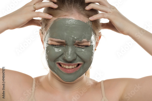 Beautiful nervous woman posing with a facial green mud mask on her face. Skin care and treatment, spa, natural beauty and cosmetology concept