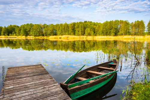 Wooden pier and fishing boat on shore of beautiful lake at sunrise, Suwalski Landscape Park, Podlasie, Poland