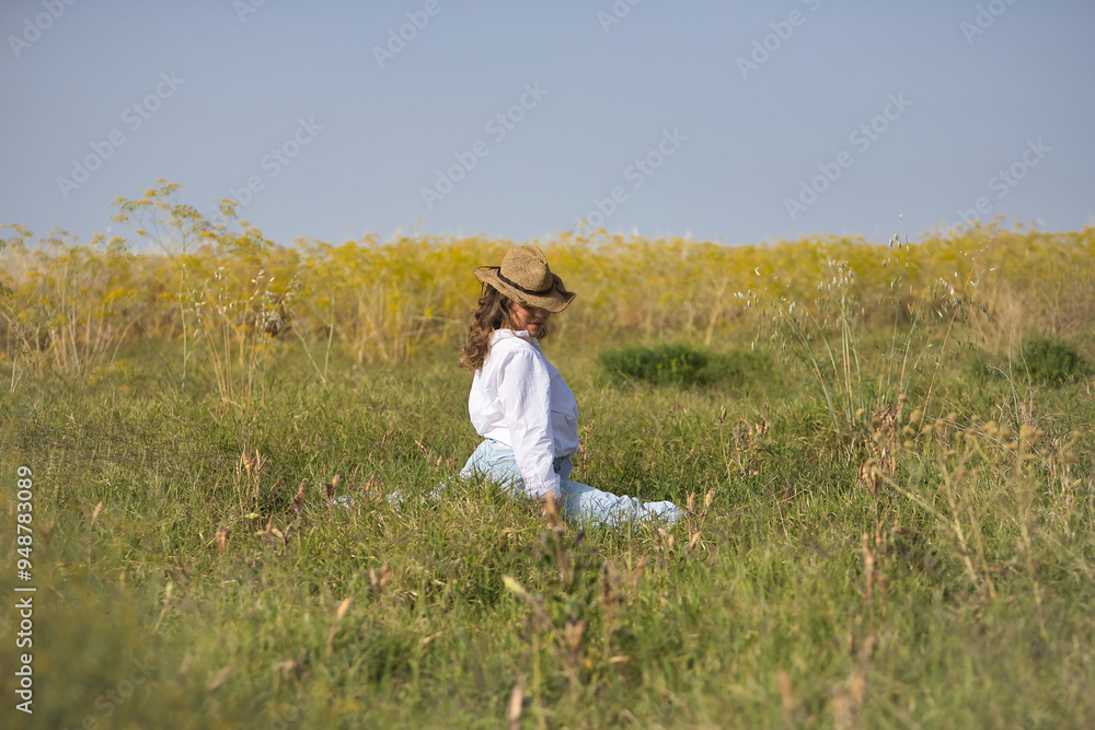 Young woman, farmer, beautiful, blonde, eyes closed, wearing a white shirt, jeans and a hat, posing with her legs spread in the middle of a field. Concept beauty, happiness, countryside, nature. Young woman, farmer, beautiful, blonde, eyes closed, wearing a white shirt, jeans and a hat, posing with her legs spread in the middle of a field. Concept beauty, happiness, countryside, nature.