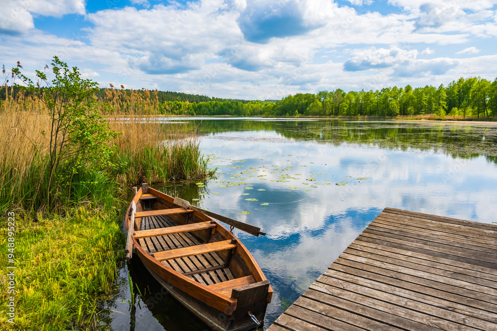 Fishing boat anchoring by wooden pier at beautiful lake, Suwalski Landscape Park, Podlasie, Poland Fishing boat anchoring by wooden pier at beautiful lake, Suwalski Landscape Park, Podlasie, Poland