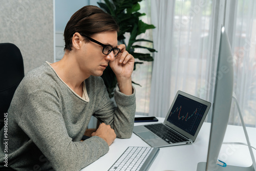 Stressful businessman casual day looking on dynamic stock exchange market graph on pc screen at modern office, analyzing to compare with database computer and laptop at working from home. Pecuniary.