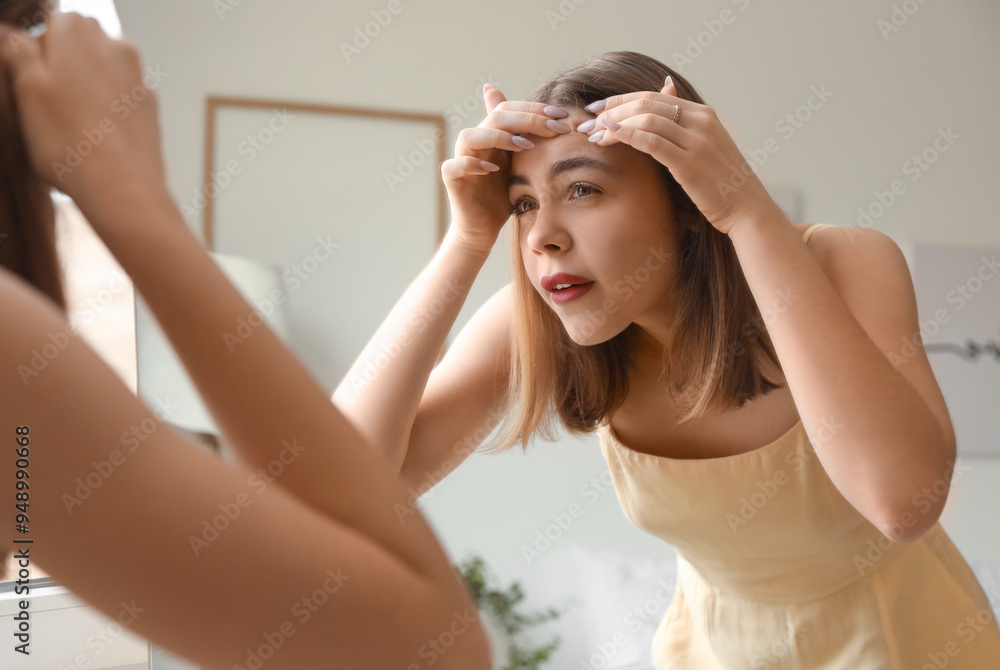 Young woman squishing pimple in front of mirror at home Young woman squishing pimple in front of mirror at home