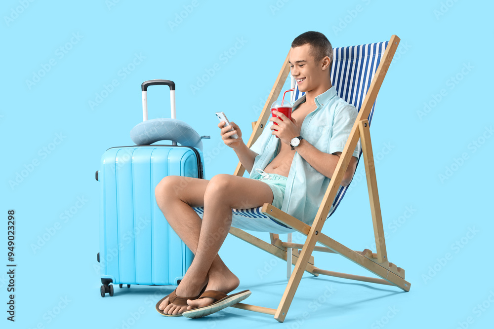 Teenage boy with soda using mobile phone in deck chair on blue background Teenage boy with soda using mobile phone in deck chair on blue background
