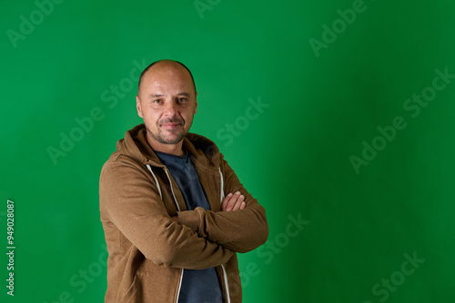 Middle aged bald man in casual attire with crossed arms poses confidently against a green studio backdrop.