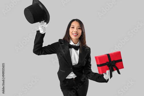 Young Asian woman dressed as magician with Halloween gift on light background