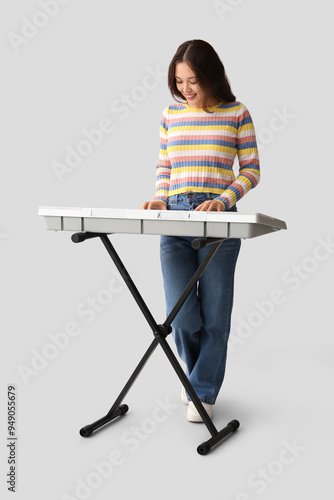 Young woman playing synthesizer on light background