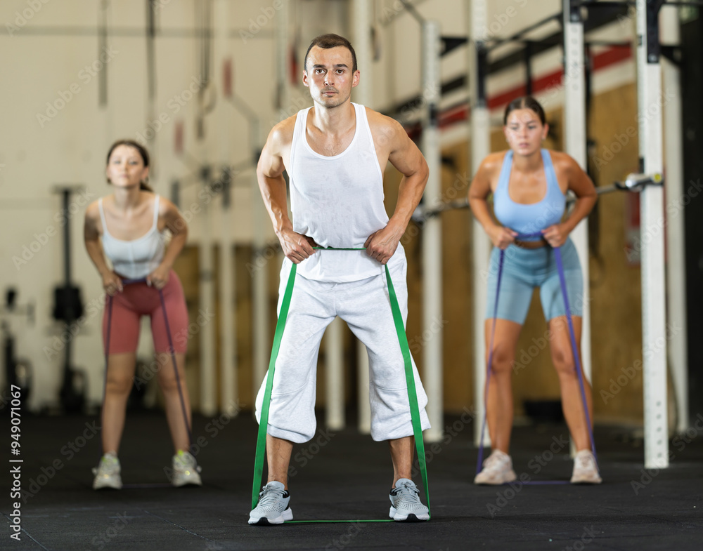 Obraz premium Active man wearing sport clothes using resistance band during group workout in gym. Functional training and CrossFit concept