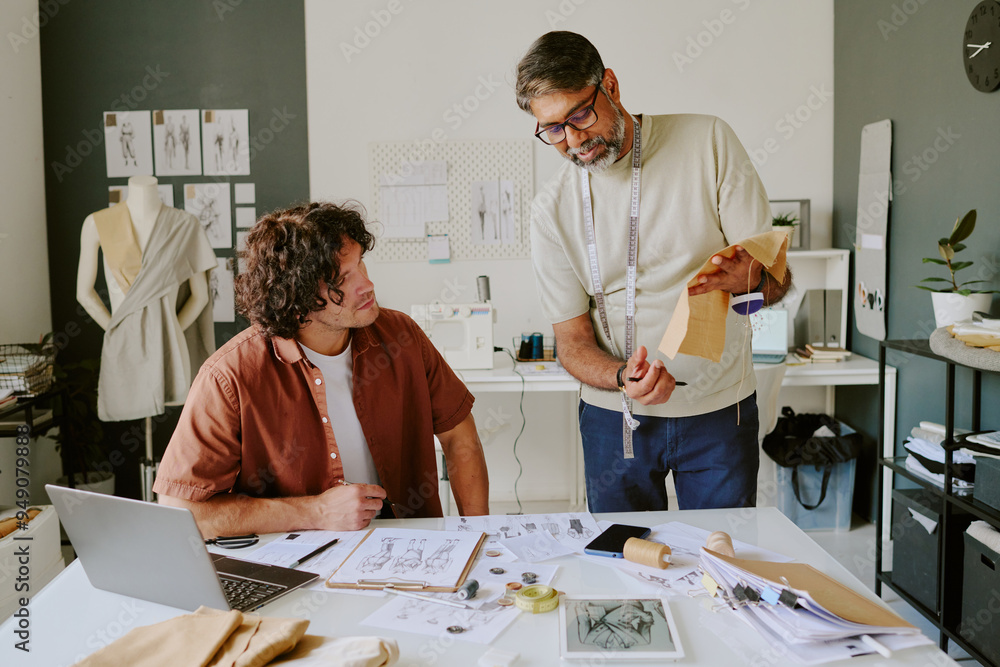 Obraz premium Mature tailor holding beige piece of fabric while his designer looking at it