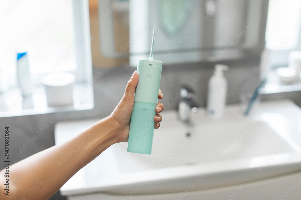 Young woman holding domestic dental water flosser in front of bathroom wash basin, pov view shot Young woman holding domestic dental water flosser in front of bathroom wash basin, pov view shot