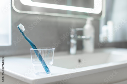 Closeup pf glass cup and toothbrush placed on washbasin in bathroom interior with grey tile walls photo